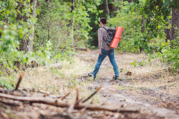 コンセプト息をのむような旅と冒険。バックビューハイキング勇敢な白人の男バックパックは、田舎道に沿って森に歩きます。テーマ観光とアウトドア活動。バックパッカーは森を通過します - 写真・画像