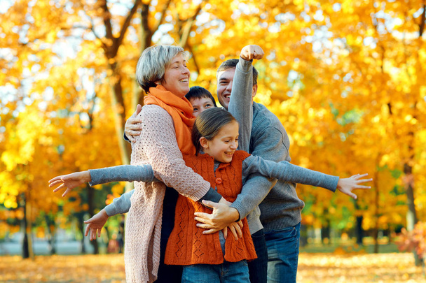 Familia feliz posando, jugando y divirtiéndose en el parque de otoño de la ciudad. Los niños y los padres juntos tienen un buen día. Luz del sol brillante y hojas amarillas en los árboles, temporada de otoño
. - Foto, Imagen