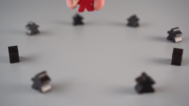 Ręka ustawia czerwoną figurę otoczoną czarnymi postaciami na szarej powierzchni. Koncepcja lidera zespołu - Materiał filmowy, wideo