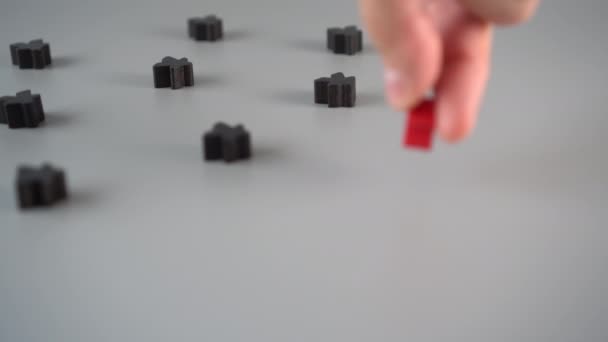 A hand sets a red figure surrounded by black figures on a gray surface. Team Leader Concept - Felvétel, videó