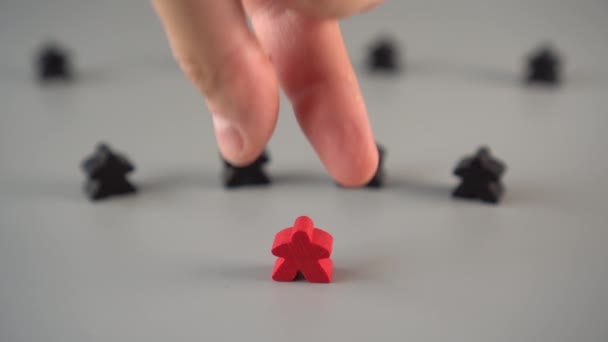 De hand verwijdert de rode figuur uit de omgeving van zwarte figuren op een grijs oppervlak. Het concept van het ontslag van de leider uit het team - Video
