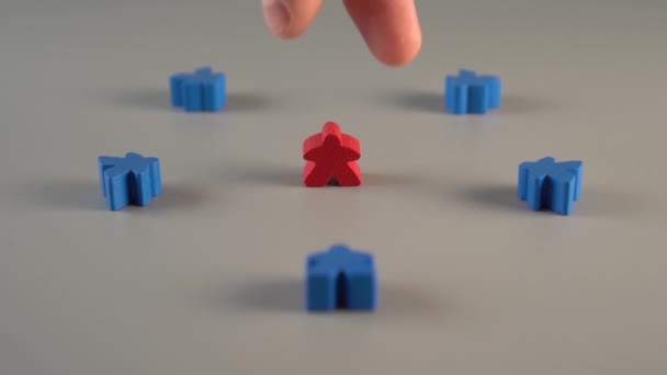 Een hand verwijdert een rode vorm uit de omgeving van blauwe vormen op een grijs oppervlak. Concept van het afvuren van een leider vanuit een team - Video
