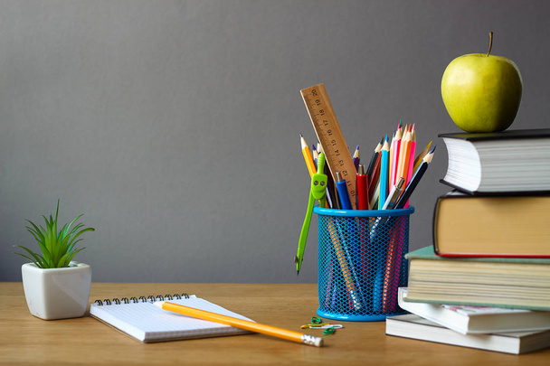 Back to school concept, school supplies, stack of books, green apple, succulent in a white pot and an open notebook on a wooden surface, selective focus - Photo, image