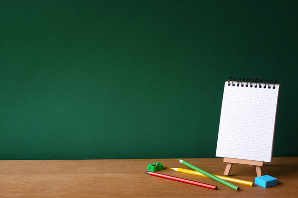 Concept de retour à l'école, carnet ouvert sur chevalet miniature et plusieurs crayons de couleur sur une surface en bois sur fond de tableau vert propre, mise au point sélective, espace de copie
 - Photo, image