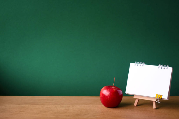 Terug naar school concept, open notitieboekje op miniatuur ezel en rode appel op houten oppervlak op de achtergrond van een schoon groen krijtbord, selectieve focus, kopieer ruimte - Foto, afbeelding