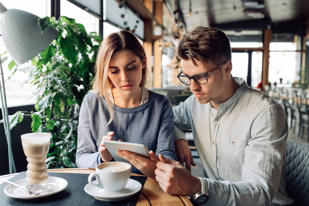 Young man and woman looking at tablet, sitting at cafe - Фото, изображение