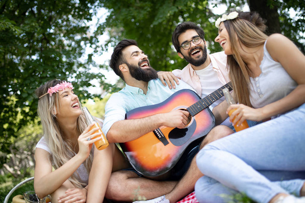 Happy young friends having picnic in the park. People ,having fun, smiling, playing guitar concept - Photo, Image
