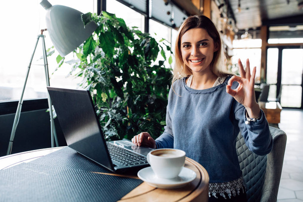 Cheerful girl showing ok sign, sitting at cafe with laptop - Foto, Imagen