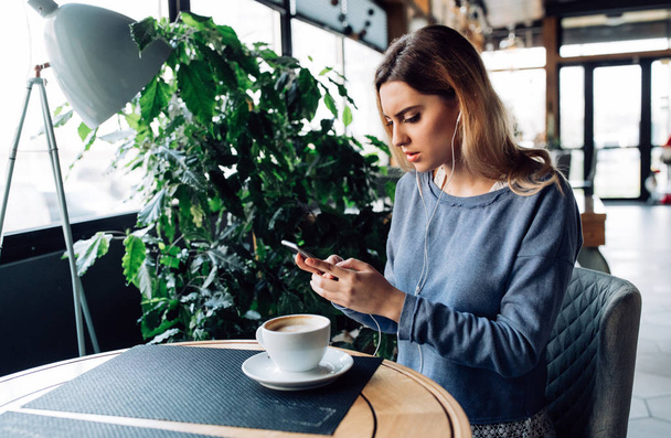 Mujer concentrada en auriculares usando teléfono inteligente mientras está sentada en
  - Foto, imagen