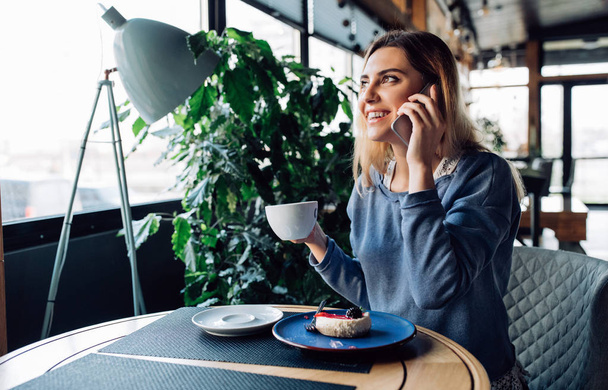 Smiling girl having phone conversation, while sitting at cafe - Foto, imagen