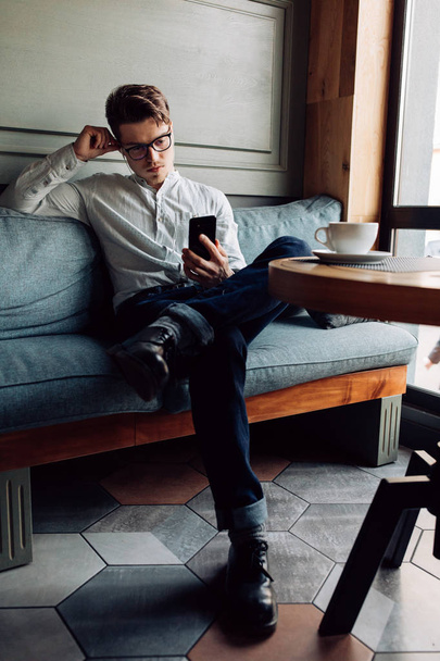 Stylish man using a smartphone, sitting on couch at cafe - Zdjęcie, obraz
