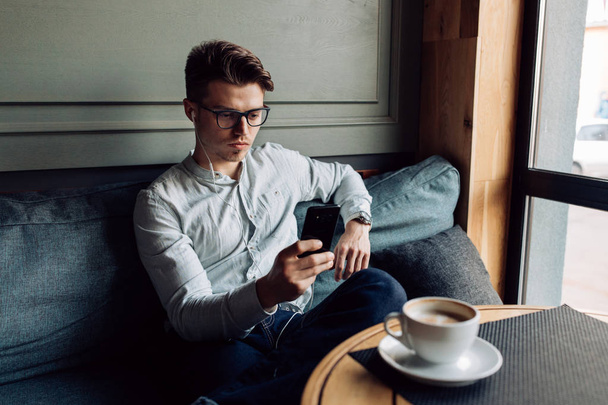 Hombre seguro usando el teléfono móvil mientras descansa en la cafetería
 - Foto, Imagen