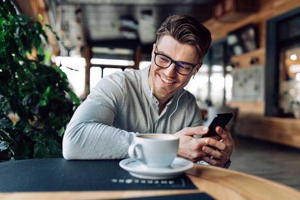 Happy guy listening to music in earphones, spending time at cafe - Fotografie, Obrázek