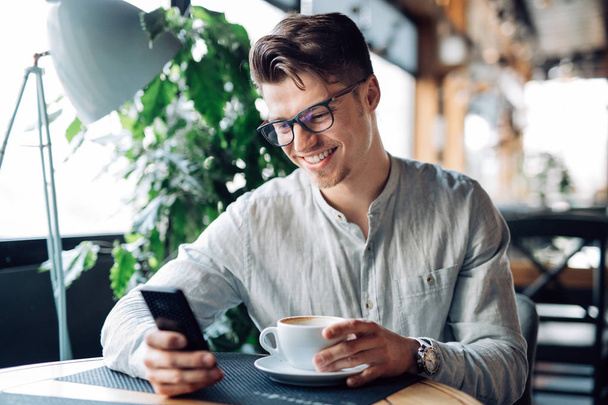 Smiling man looking at smartphone screen while resting at cafe - Foto, Bild