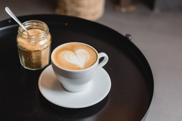 Jeden šálek cappuccina s Latte art na černém stole, bílý keramický pohár, vrcholný výhled. Cafe kultura. - Fotografie, Obrázek
