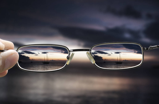 Sonnenuntergang am Meer mit einer Brille in der Hand, die die Sicht korrigiert - Foto, Bild
