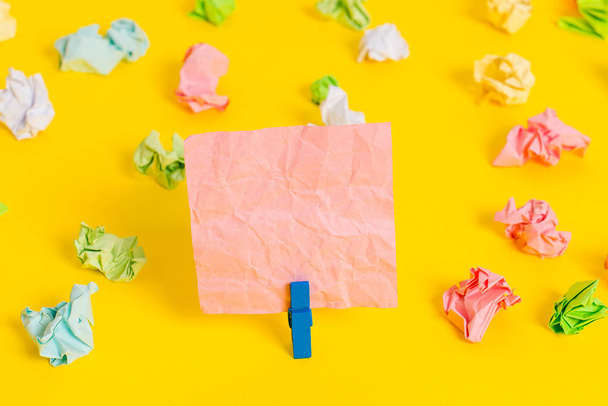 Colored crumpled sheets placed around the empty rectangle square shaped reminder note in the yellow background. Office supplies, blank paper pinned by a fastener. - 写真・画像