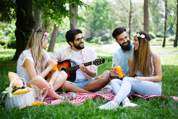 Happy young friends having picnic in the park. People ,having fun, smiling, playing guitar concept - Foto, imagen