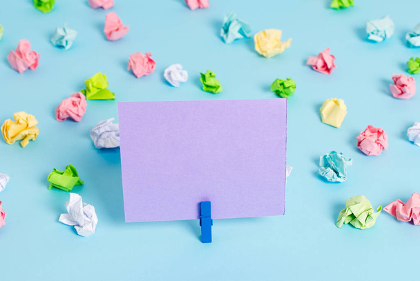 Colored crumpled sheets placed around the empty rectangle square shaped reminder note in the blue background. Office supplies, blank paper pinned by a fastener. - Фото, изображение
