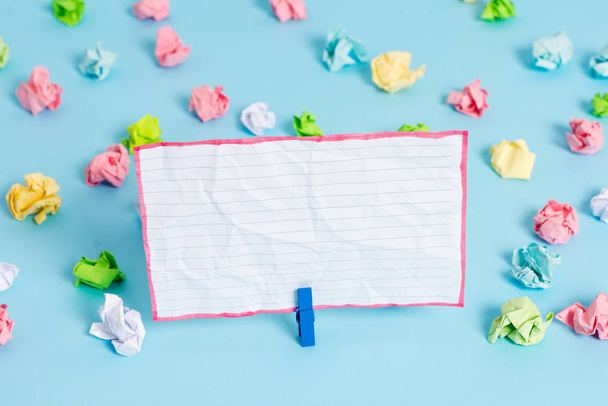 Colored crumpled sheets placed around the empty rectangle square shaped reminder note in the blue background. Office supplies, blank paper pinned by a fastener. - Photo, Image