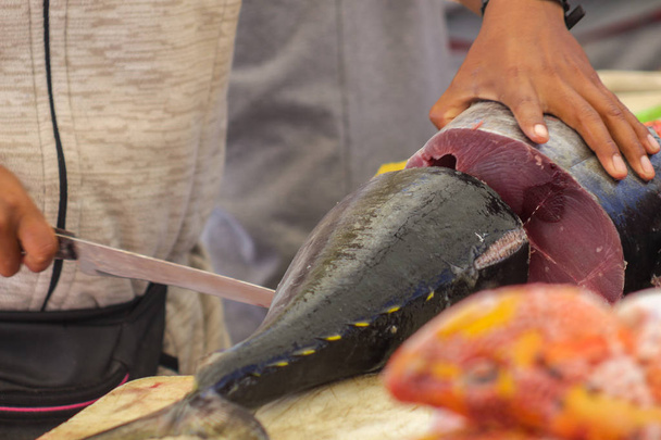 Primer plano de las manos de un pescador que filetea un atún para la venta
 - Foto, Imagen