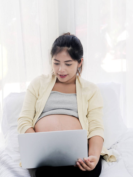 Asiatique femme enceinte en utilisant ordinateur portable sur le lit à la maison, style de vie conc
 - Photo, image