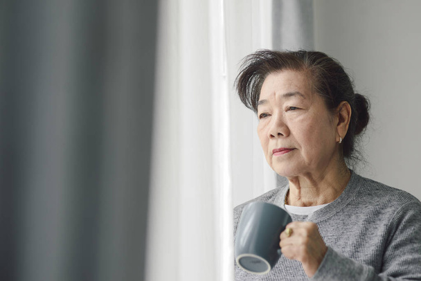 Asian senior woman drinking hot tea near window outdoor, lonely  - Photo, image