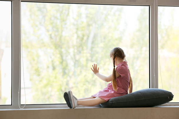 Malá holčička s autistickou poruchou sedící na okenní parapetu doma - Fotografie, Obrázek