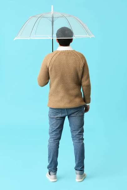 Hombre joven guapo con paraguas en el fondo de color, vista posterior - Foto, imagen