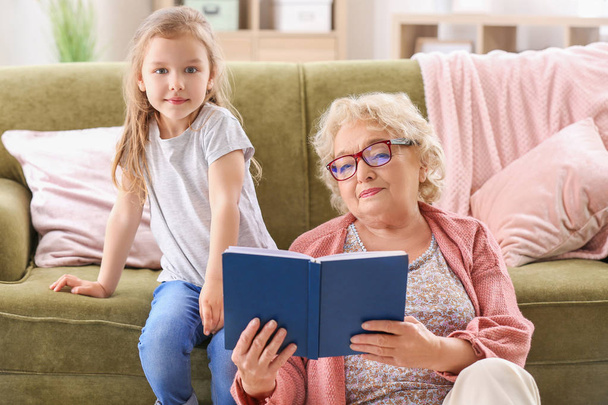 Χαριτωμένο μικρό κορίτσι διαβάζοντας το βιβλίο με τη γιαγιά στο σπίτι - Φωτογραφία, εικόνα