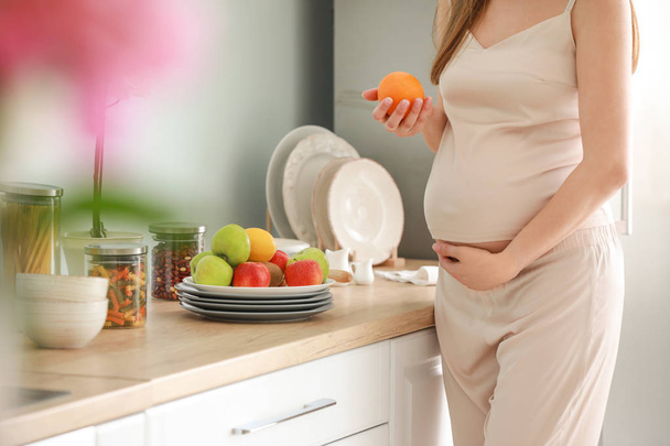 Beautiful pregnant woman with fruits in kitchen - Foto, imagen