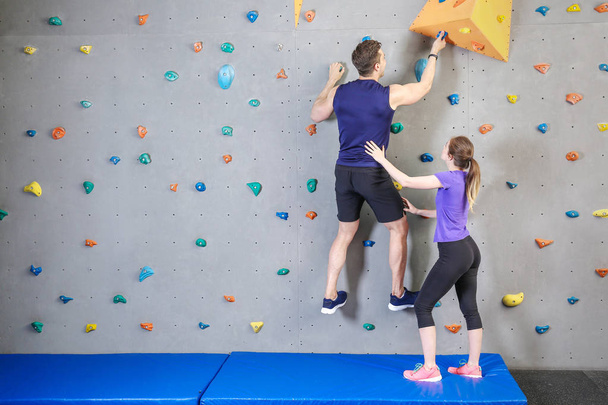 Genç adama spor salonunda duvara tırmanmayı öğreten eğitmen - Fotoğraf, Görsel
