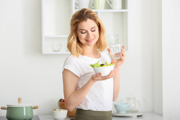 Vrouw met gezonde groente salade en glas water in de keuken - Foto, afbeelding