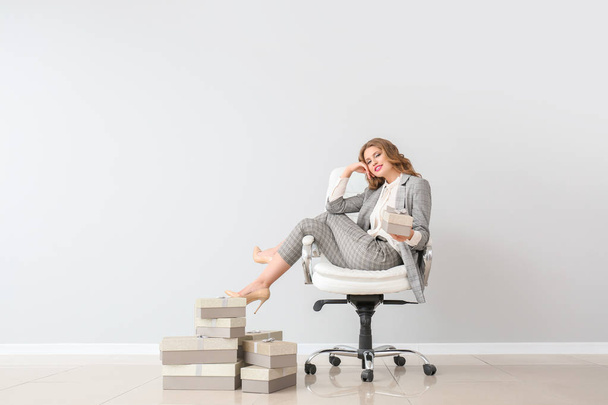 Mulher bonita com caixas de presente sentadas na cadeira contra parede leve
 - Foto, Imagem