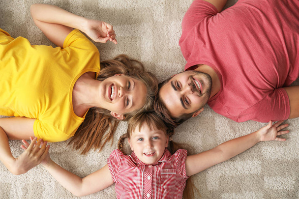 Портрет счастливой молодой семьи, лежащей дома на ковре
 - Фото, изображение