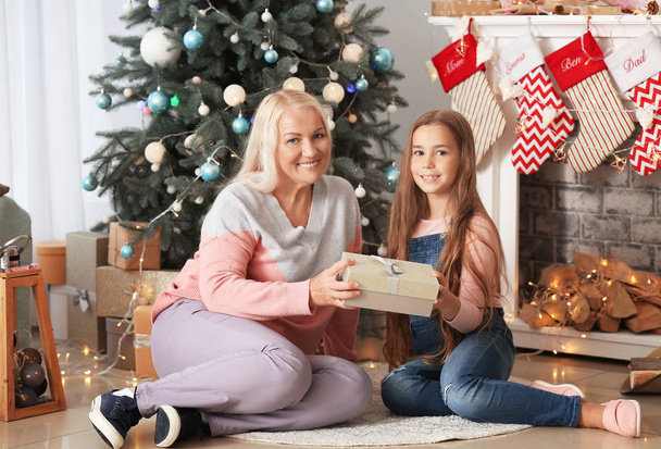 Onnellinen isoäiti ja pieni tyttö lahjapakkauksella huoneessa koristeltu jouluksi
 - Valokuva, kuva
