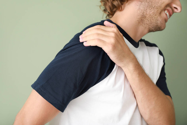 Young man suffering from pain in shoulder on color background - Photo, Image