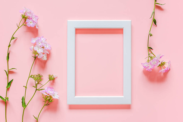 White wooden picture frame and flowers on pink background with copy space. Creative Top view Flat lay Mock up Template for invitstion, greeting card - 写真・画像
