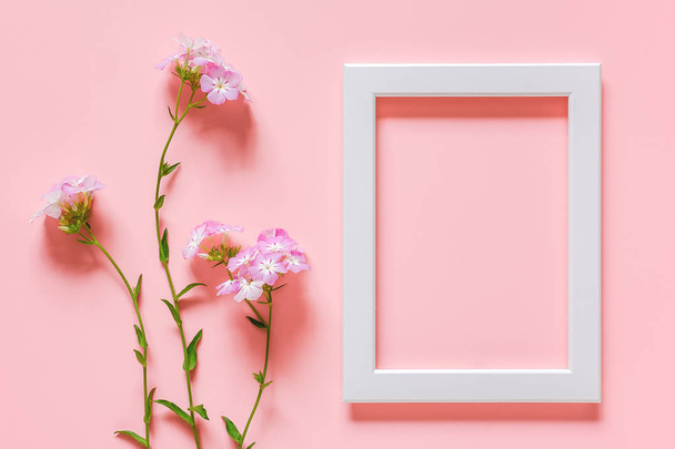 White wooden picture frame and flowers on pink background with copy space. Creative Top view Flat lay Mock up Template for invitstion, greeting card - Foto, Bild