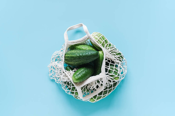 Fresh green cucumbers vegetables in reusable shopping eco-frendly mesh bag on blue background. Concept no plastic and zero waste. Copy space Top view Flat lay - Фото, изображение