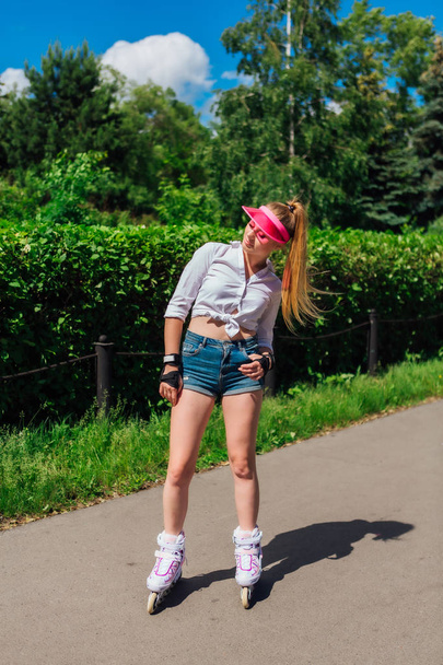 Portrait of an emotional girl in a pink cap visor and protective gloves for rollerblades and skateboarding riding on rollerblades on the road. - Photo, Image