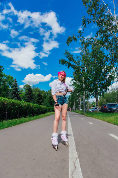 Portrait of an emotional girl in a pink cap visor and protective gloves for rollerblades and skateboarding riding on rollerblades on the road. - Foto, Imagem