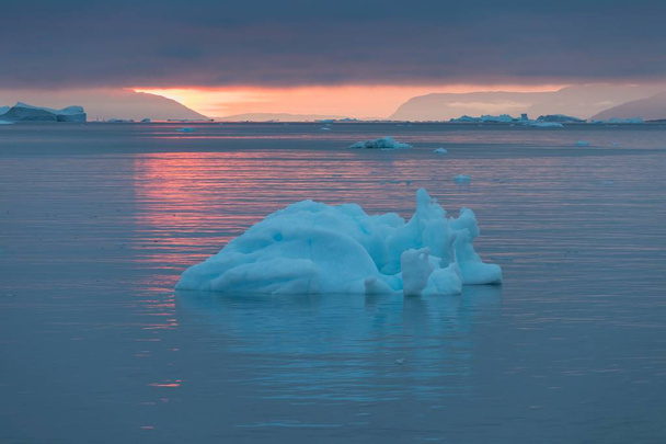 地平線に真夜中の日没/日の出とグリーンランドアイスフィヨルドの氷山と北極の自然の風景。真夜中の季節の早朝の夏のアルペングロー。イリッサット (西グリーンランド). - 写真・画像