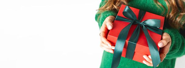 Woman in green woolen sweater holding present red gift box with green bow on white background - Fotoğraf, Görsel