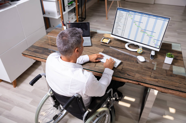 Handicapped Businessman Sitting On Wheelchair And Using Computer In Office - Фото, изображение