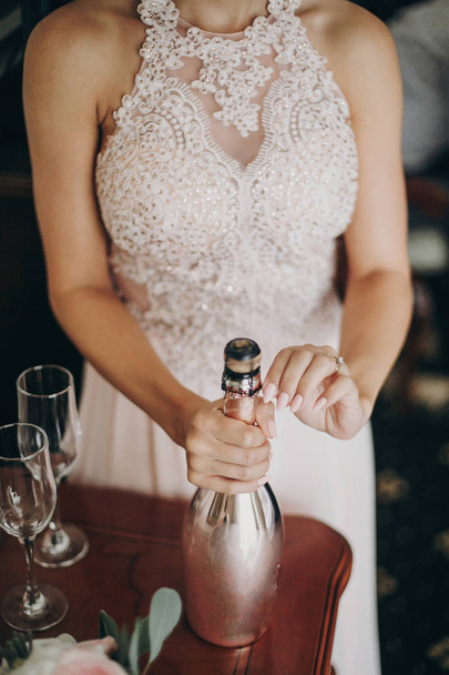 Stylish bride or bridesmaids opening champagne bottle for celebr - Фото, изображение