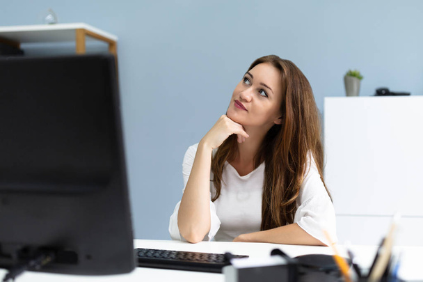 Smiling Young Businesswoman Daydreaming While Sitting In Her Office Desk - Foto, imagen
