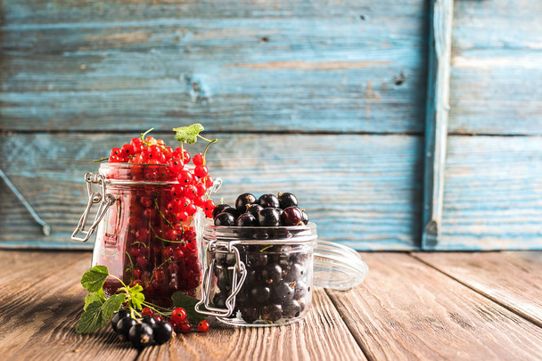Fresh ripe berries of red black currant various glass jars wooden rustic background. Horizontal frame Selective focus. - Foto, imagen