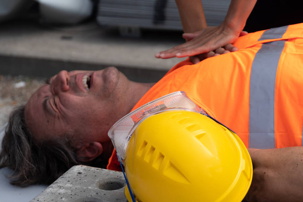 Image recadrée des mains d'un ambulancier pratiquant la réanimation cardiopulmonaire (RCR) sur un travailleur de la construction blessé dans un accident du travail
 - Photo, image