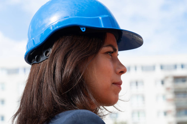 青い保護ヘルメットをかぶった女性エンジニアのプロフィールをクローズアップ - 写真・画像